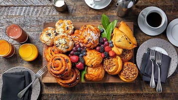 A breakfast spread with pastries, fruits, and beverages on a wooden table.