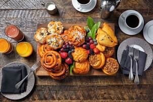 A breakfast spread with pastries, fruits, and beverages on a wooden table.