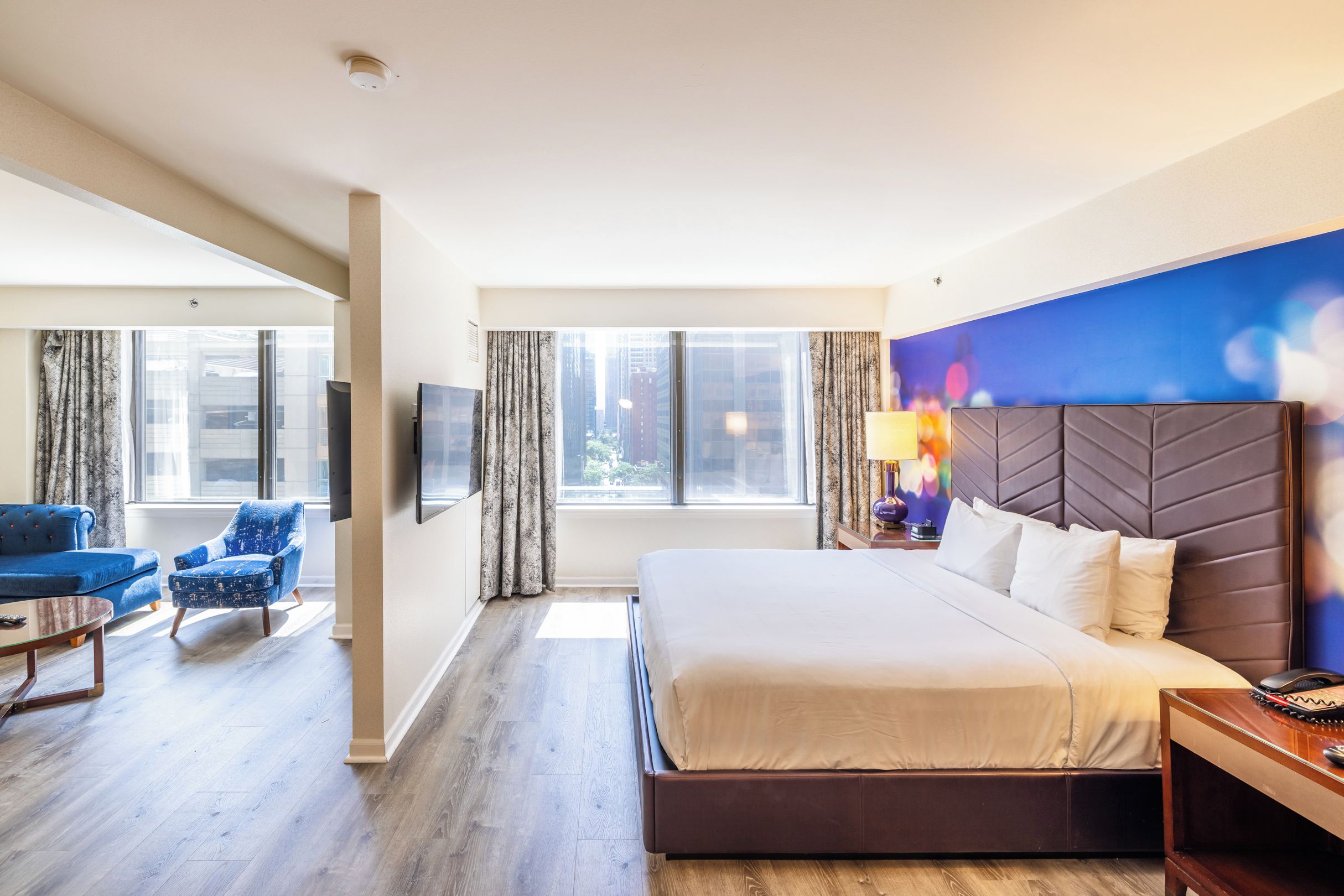 A hotel room with a large bed, a desk with a lamp, a chair, and a TV.