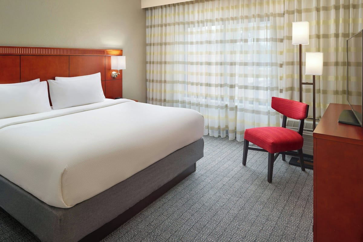 A hotel room with a large bed, a desk with a chair, and a window with curtains.