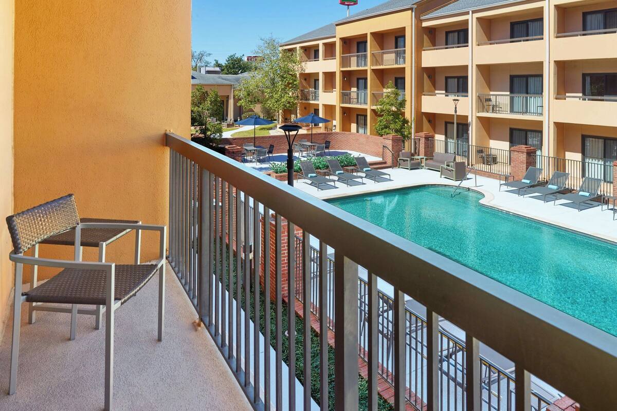 A hotel with a pool area, including lounge chairs and umbrellas, and a balcony with a chair.