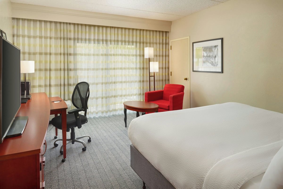 A hotel room with a large bed, a desk with a chair, a small table, and a TV.