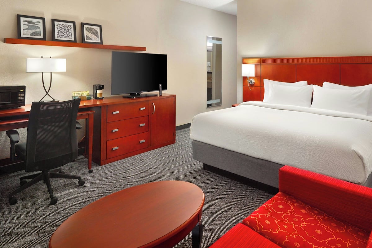 A hotel room with a bed, a desk with a television, a chair, a table, and a mirror.