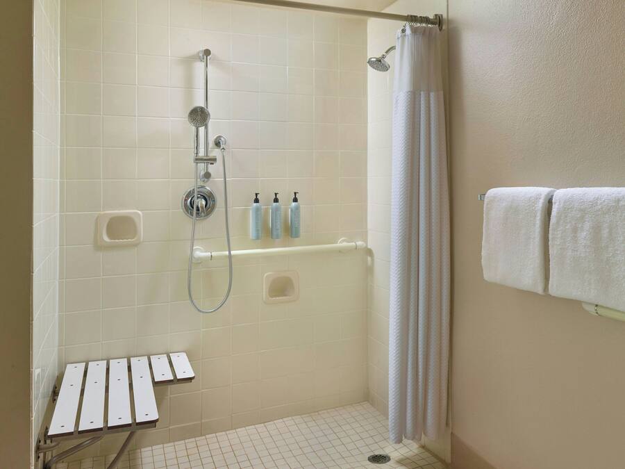 A shower area with a glass door, a hand showerhead, a handheld showerhead, and a small shelf with toiletries.