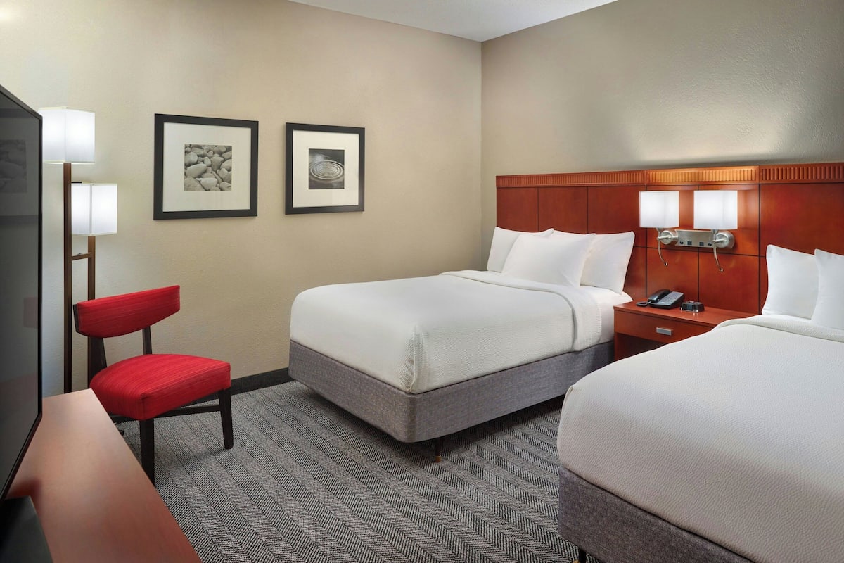 A hotel room with two beds, a desk, a chair, and two framed pictures on the wall.