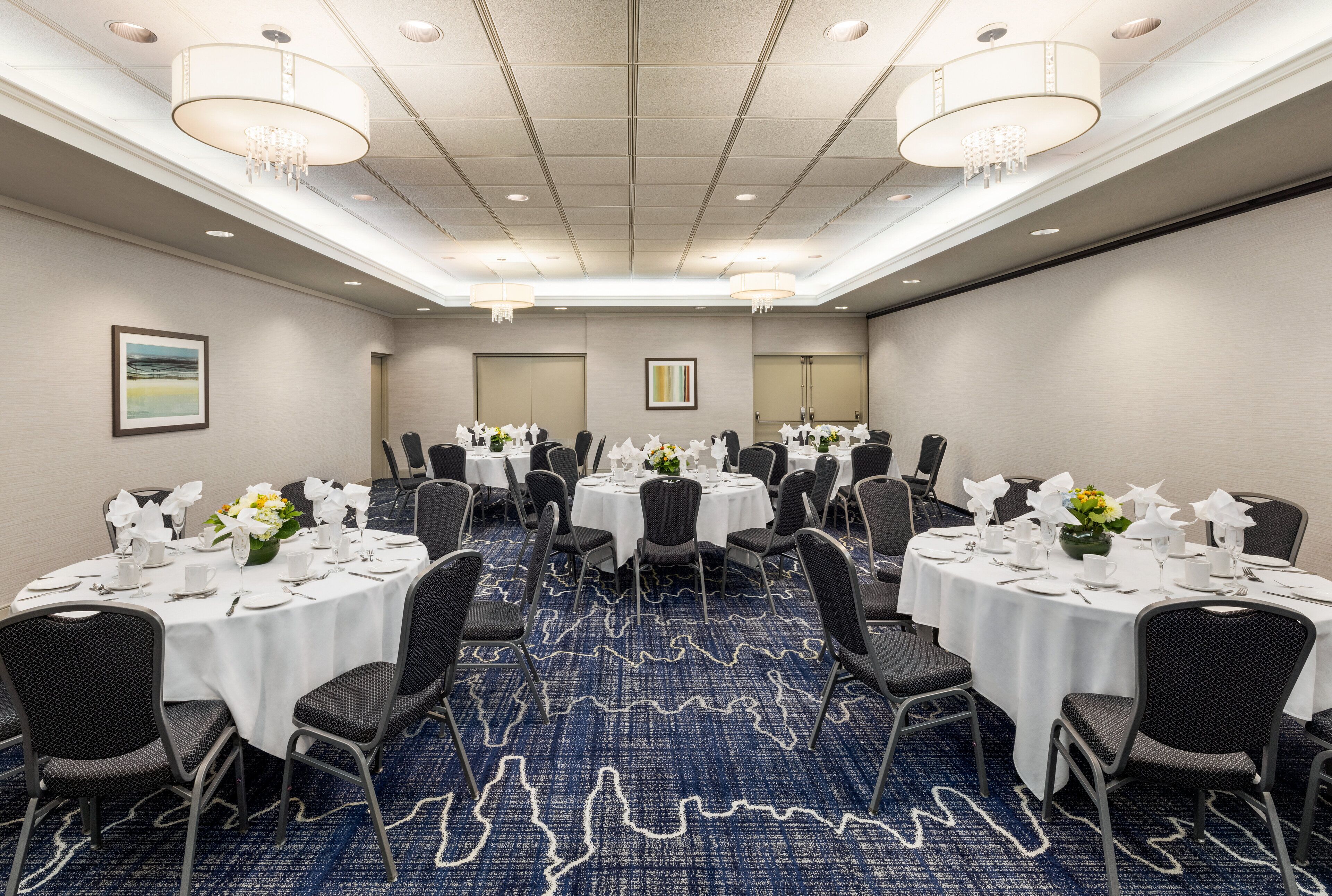 Une salle de conférence avec des tables rondes, des chaises noires, des nappes blanches et des centres de table floraux.
