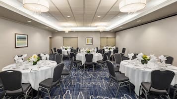 Une salle de conférence avec des tables rondes, des chaises noires, des nappes blanches et des centres de table floraux.
