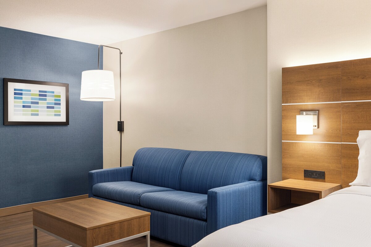 A hotel room with a blue sofa, a wooden nightstand, a white bed, and a framed picture on the wall.