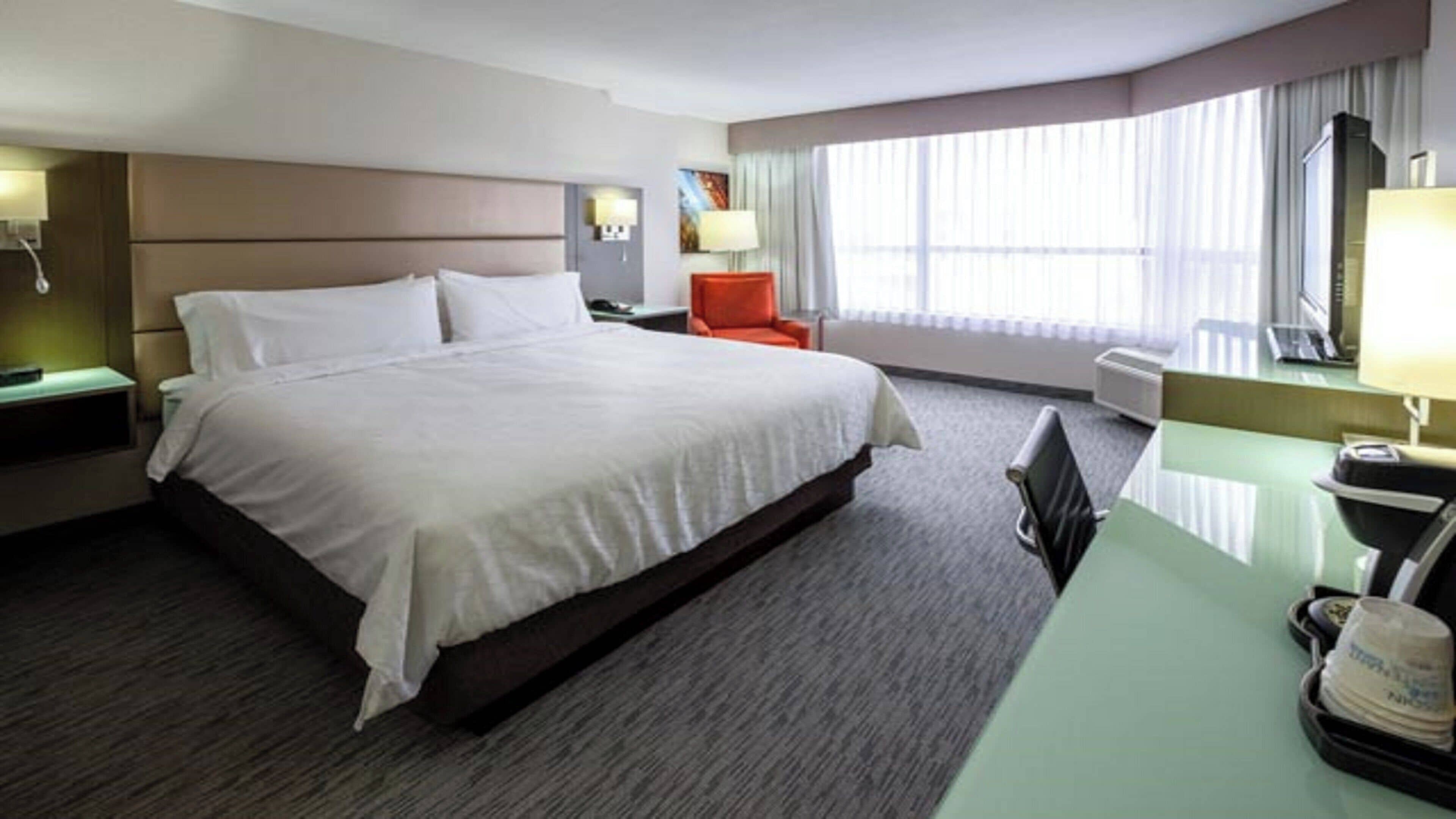 Une chambre d’hôtel avec un grand lit, un bureau, une chaise et une fenêtre avec des rideaux.