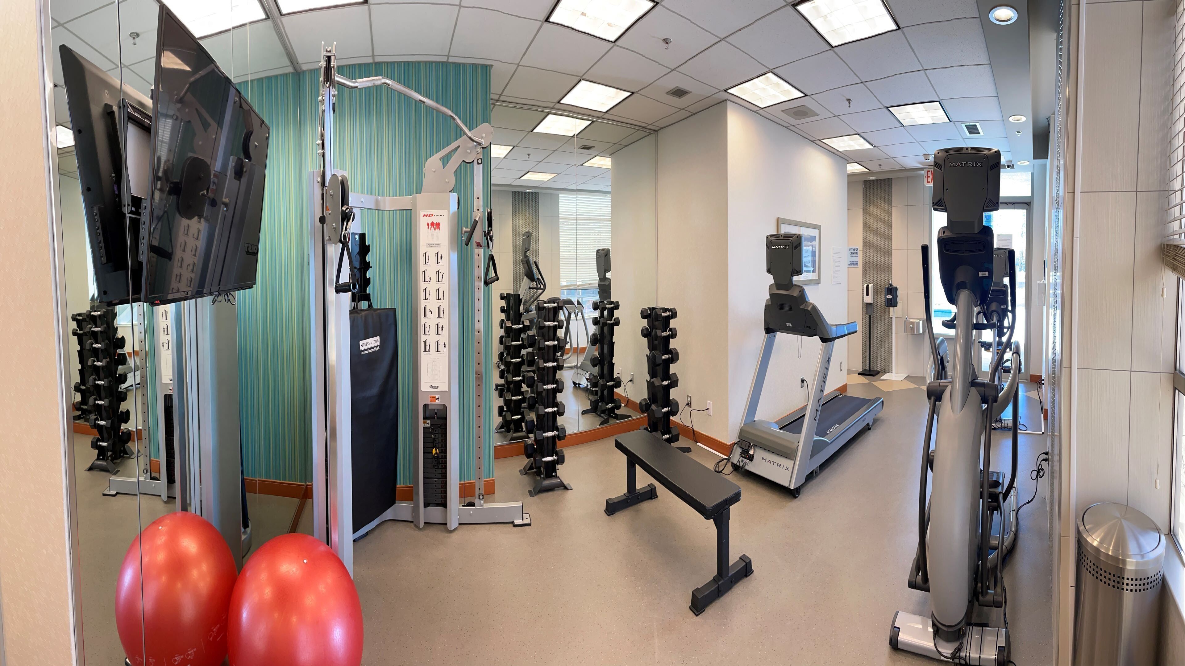 A gym with various exercise equipment, including treadmills, weight machines, and free weights.