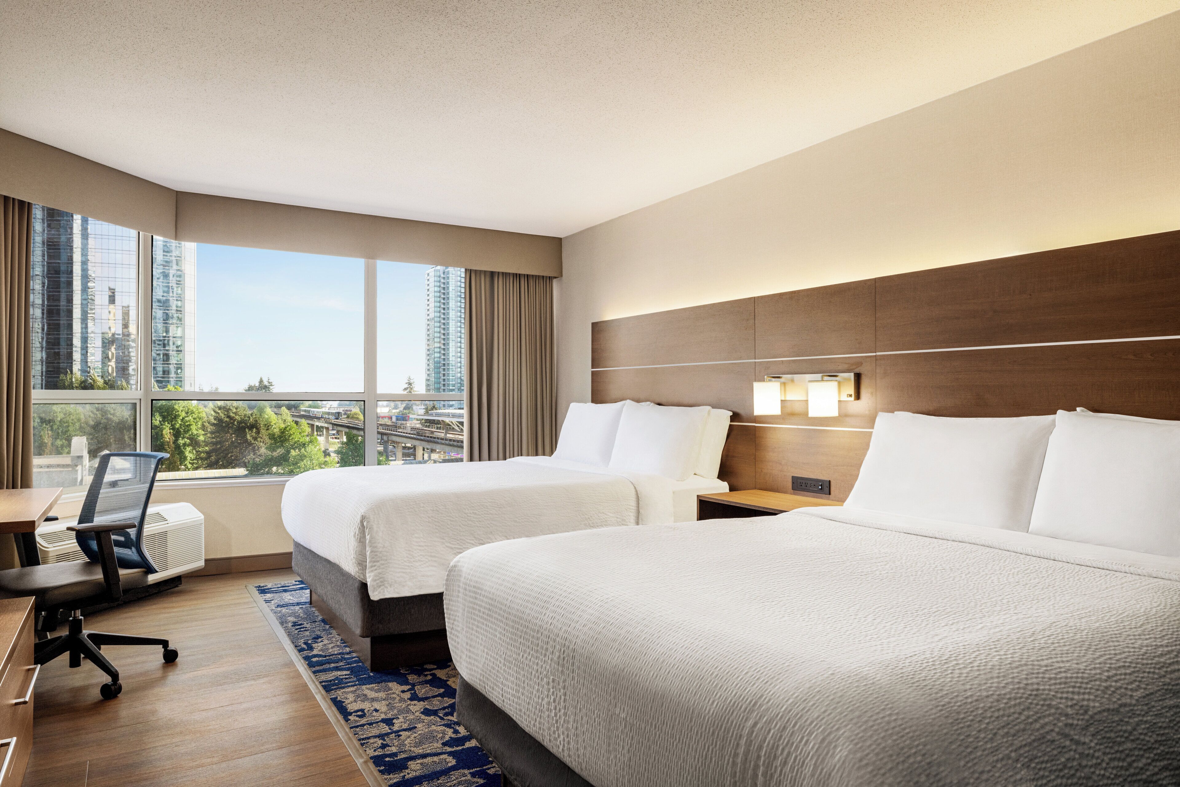 Ein Hotelzimmer mit zwei Betten, einem Schreibtisch und Blick auf die Stadt.