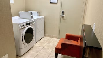A laundry room with a washing machine, dryer, and a chair.