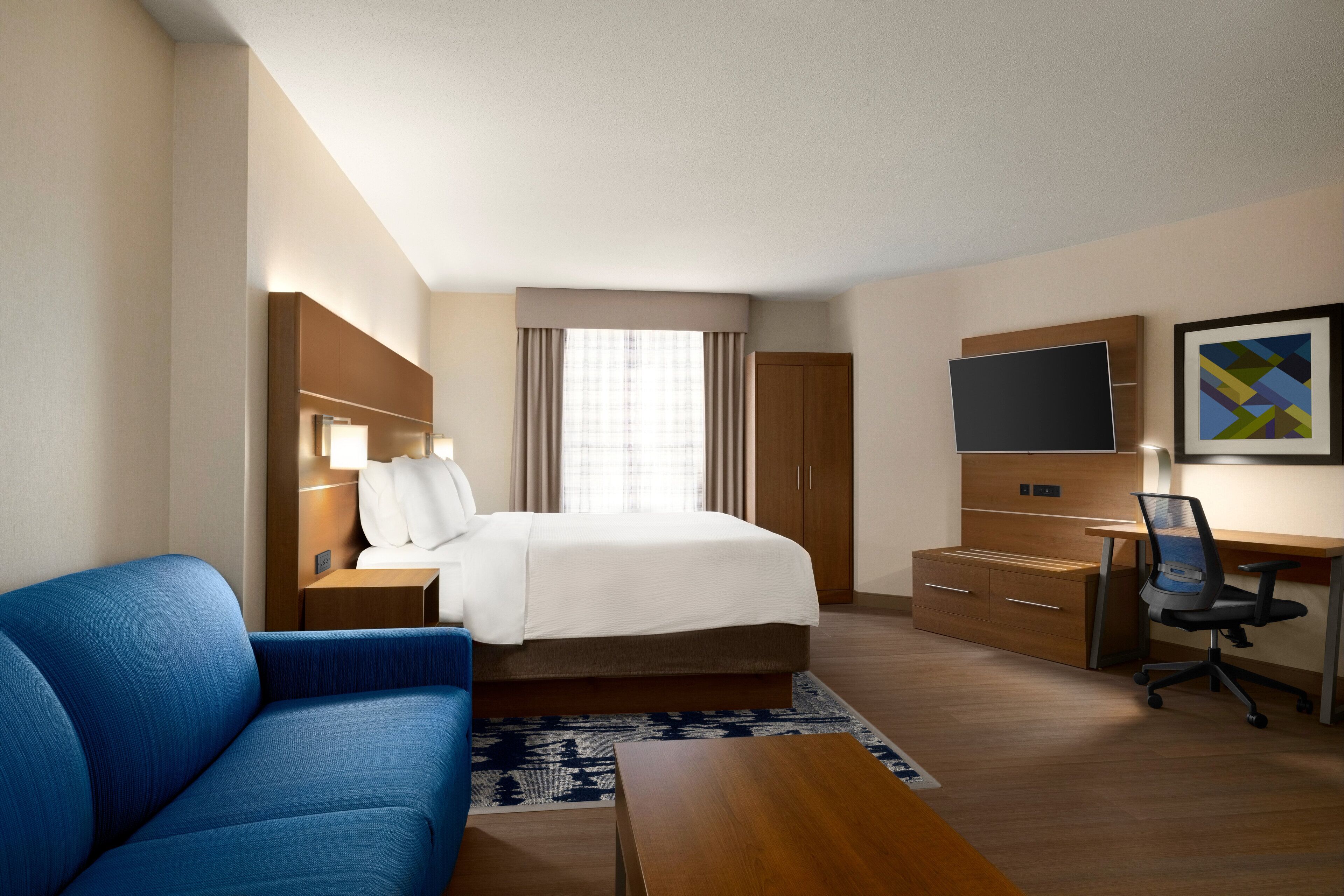 Een hotelkamer met een bed, een blauwe bank, een bureau met stoel, een televisie en een kledingkast.