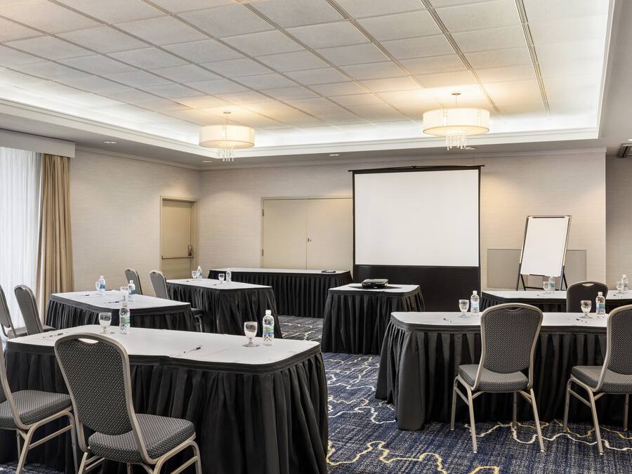 A conference room with round tables, chairs, a projector screen, and a whiteboard.