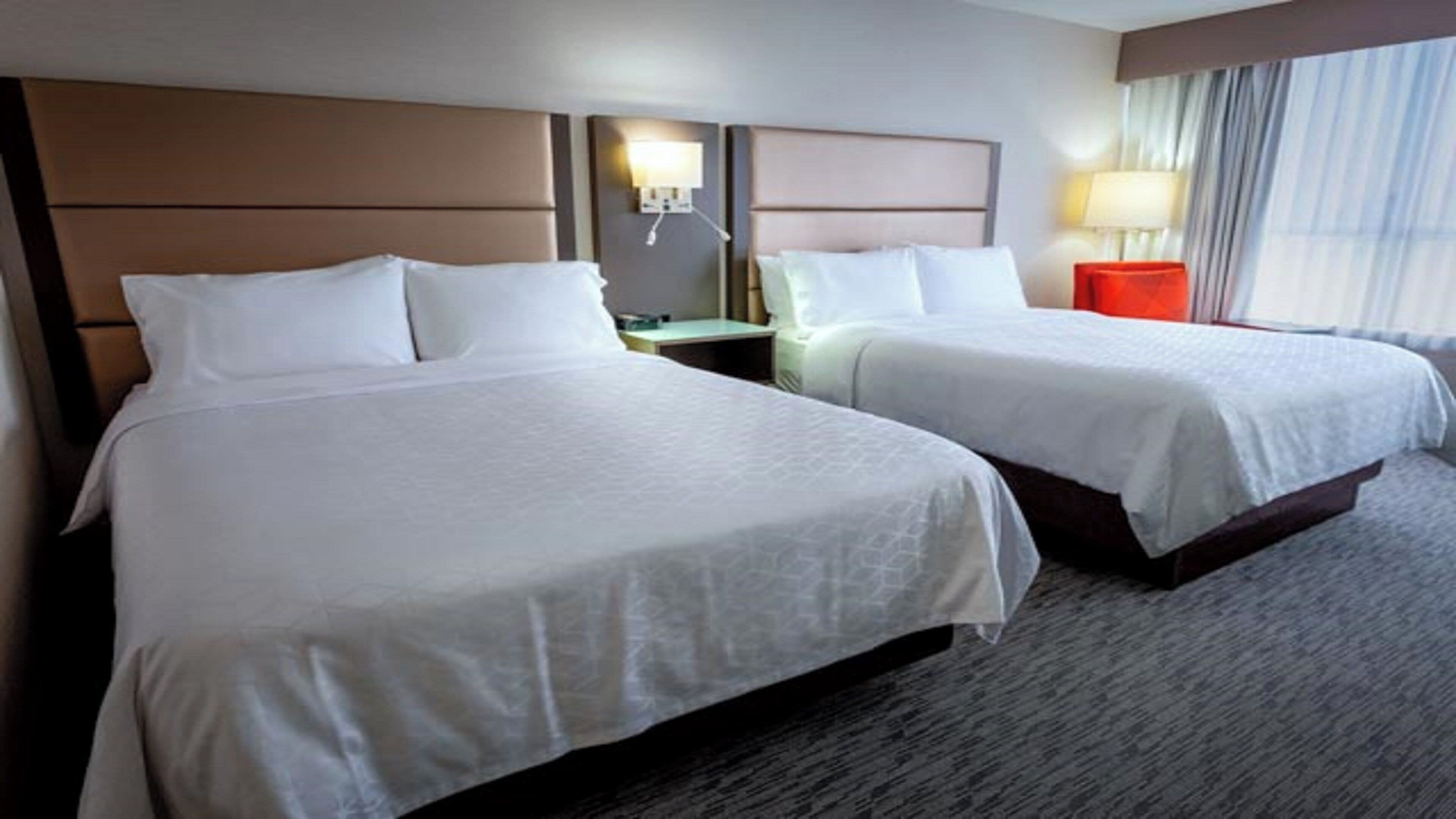 Une chambre d’hôtel avec deux lits, une table de chevet, une lampe et une fenêtre avec des rideaux.