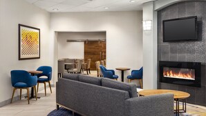 A modern lounge area with a sofa, blue chairs, a fireplace, and a flat-screen TV. - Holiday Inn Express Vancouver-Metrotown (Burnaby) by IHG (Burnaby)