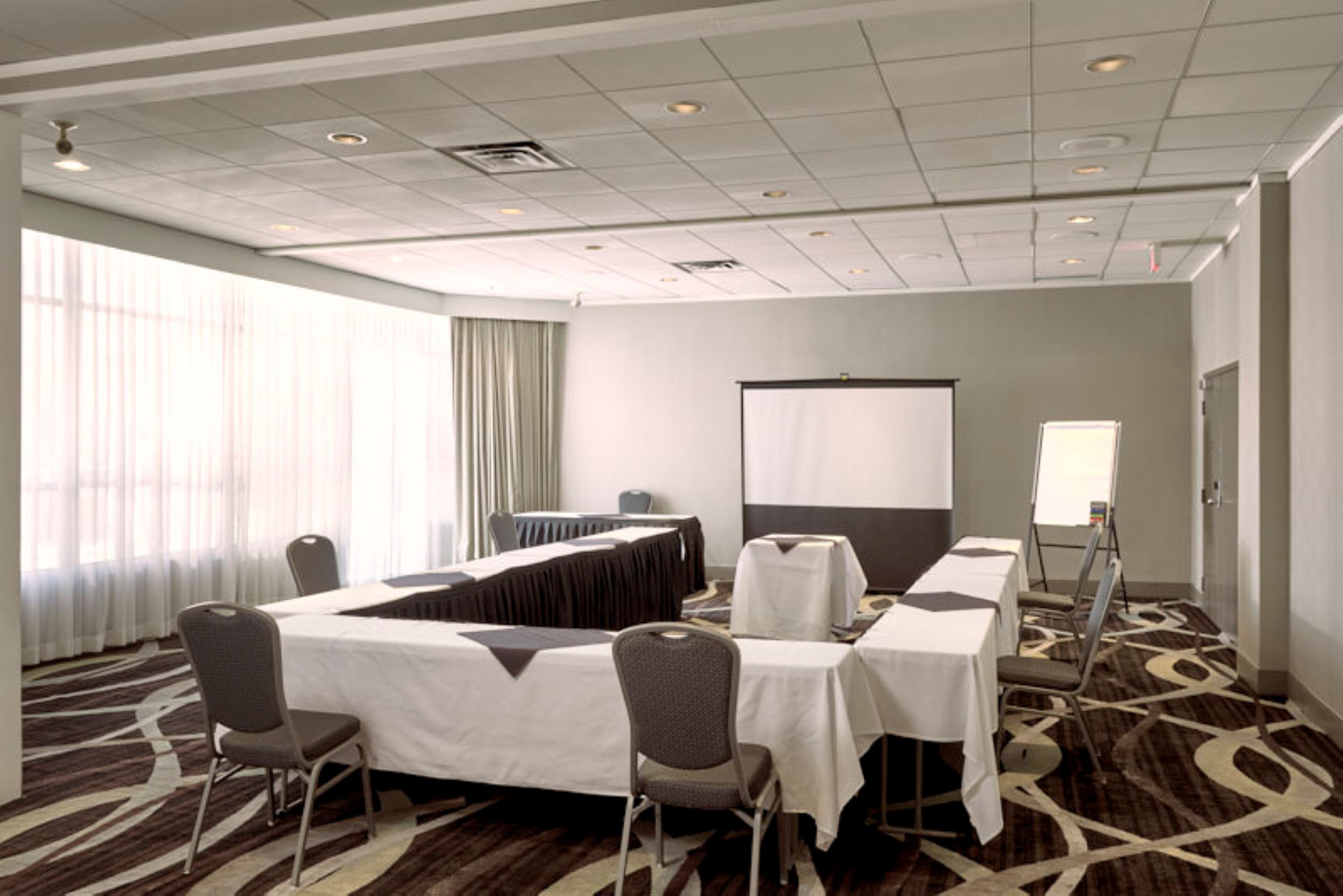 A conference room with a large table, chairs, a projector screen, and a carpeted floor.