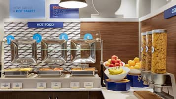 A buffet setup with labeled food stations including scrambled eggs, cheese omelet, pork sausage, bacon, turkey sausage, and baked beans.