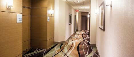 Un pasillo de hotel con paneles de madera, alfombra estampada e iluminación empotrada.