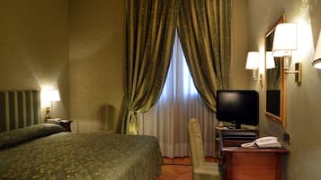 Una habitación de hotel con una cama grande, un escritorio con teléfono, televisor y espejo.