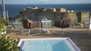 Un espace piscine aménagé sur le toit, avec deux chaises et une table, offrant une vue sur le paysage urbain et la mer.