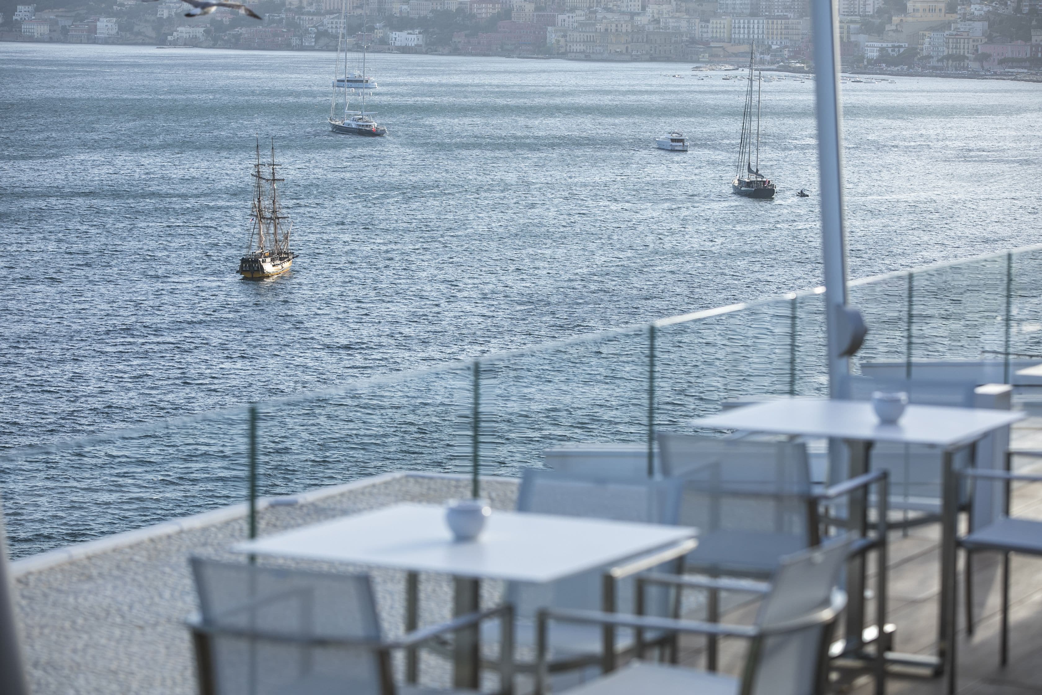 Un restaurant situé au bord de l’eau, avec une terrasse offrant une vue sur un plan d’eau où naviguent des voiliers.