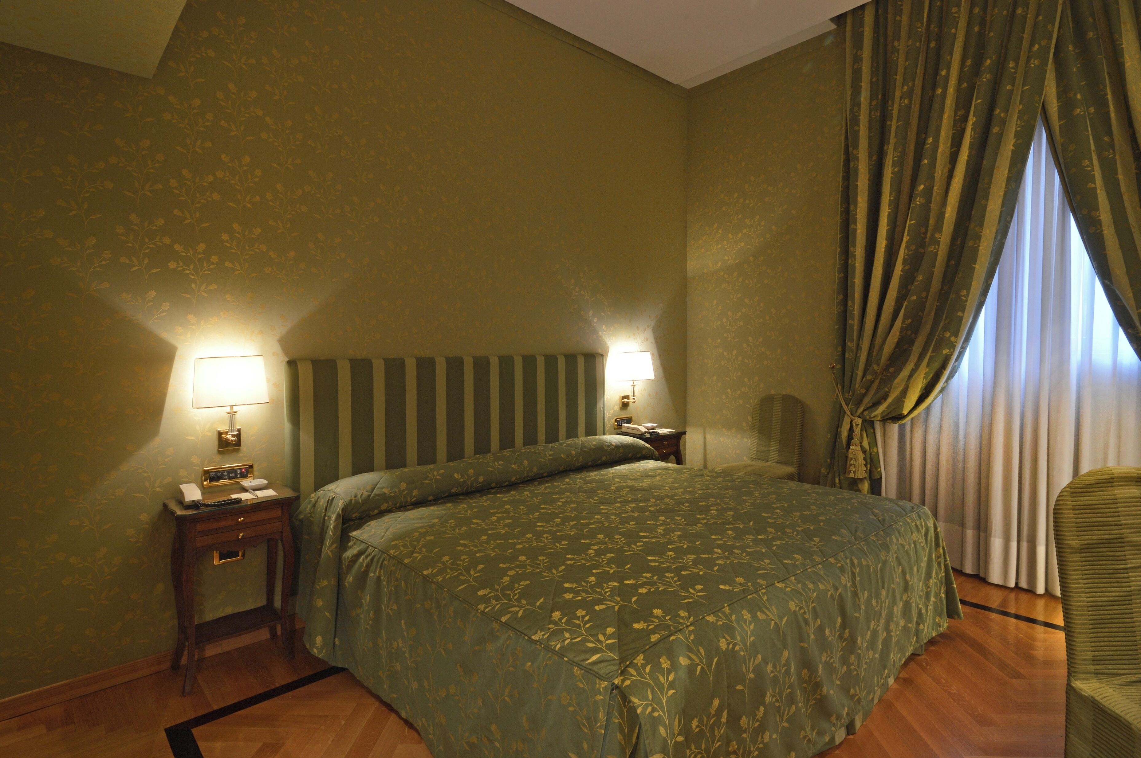 A hotel room with a large bed, two bedside lamps, a nightstand, and a chair.