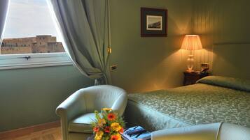 Una habitación de hotel con una cama, una silla, una mesa con un florero y una lámpara, además de un cuadro en la pared.