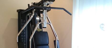 A home gym with a multi-functional exercise machine, a pull-up bar, and a bench.