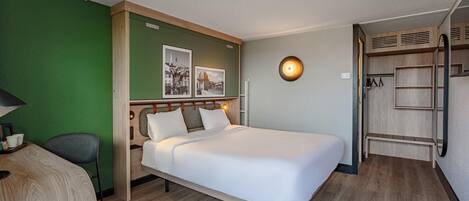 Habitación de hotel con cama, escritorio, silla, armario e iluminación de pared.