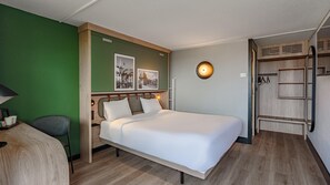 Habitación de hotel con cama, escritorio, silla, armario e iluminación de pared.