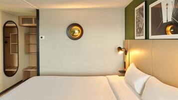 A modern hotel room with a bed, a wall-mounted circular light, a shelf unit, and a framed picture.
