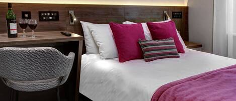 Habitación de hotel con cama, escritorio, silla, botella de vino y dos copas de vino.