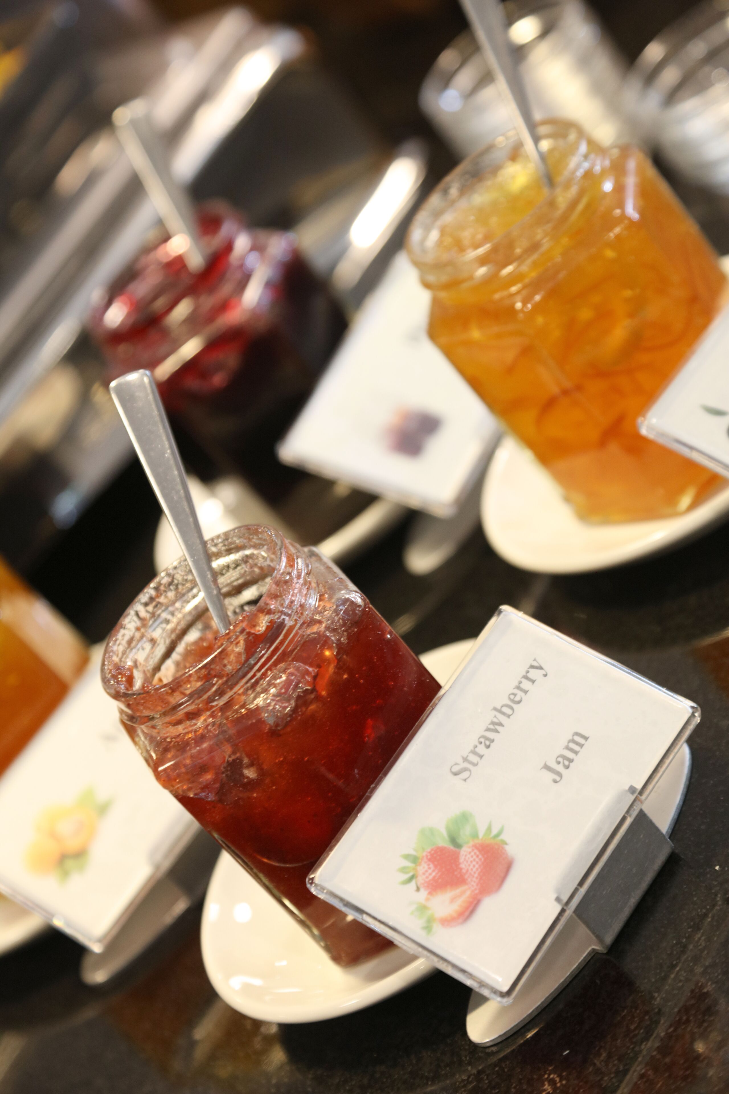 A selection of jams with labels, including strawberry and jam, on a tray.