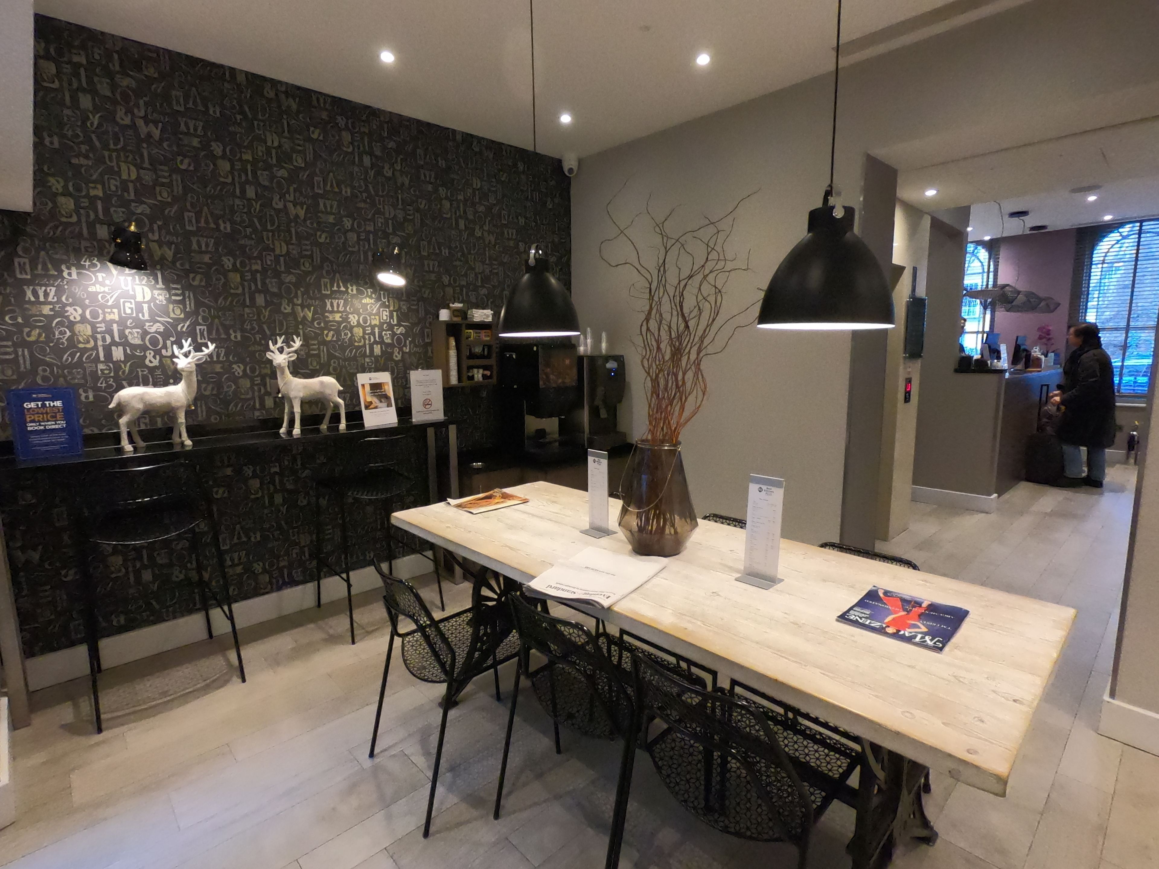 Un comedor moderno con una mesa larga, sillas negras e iluminación colgante. Hay figuritas decorativas de ciervos en la encimera.