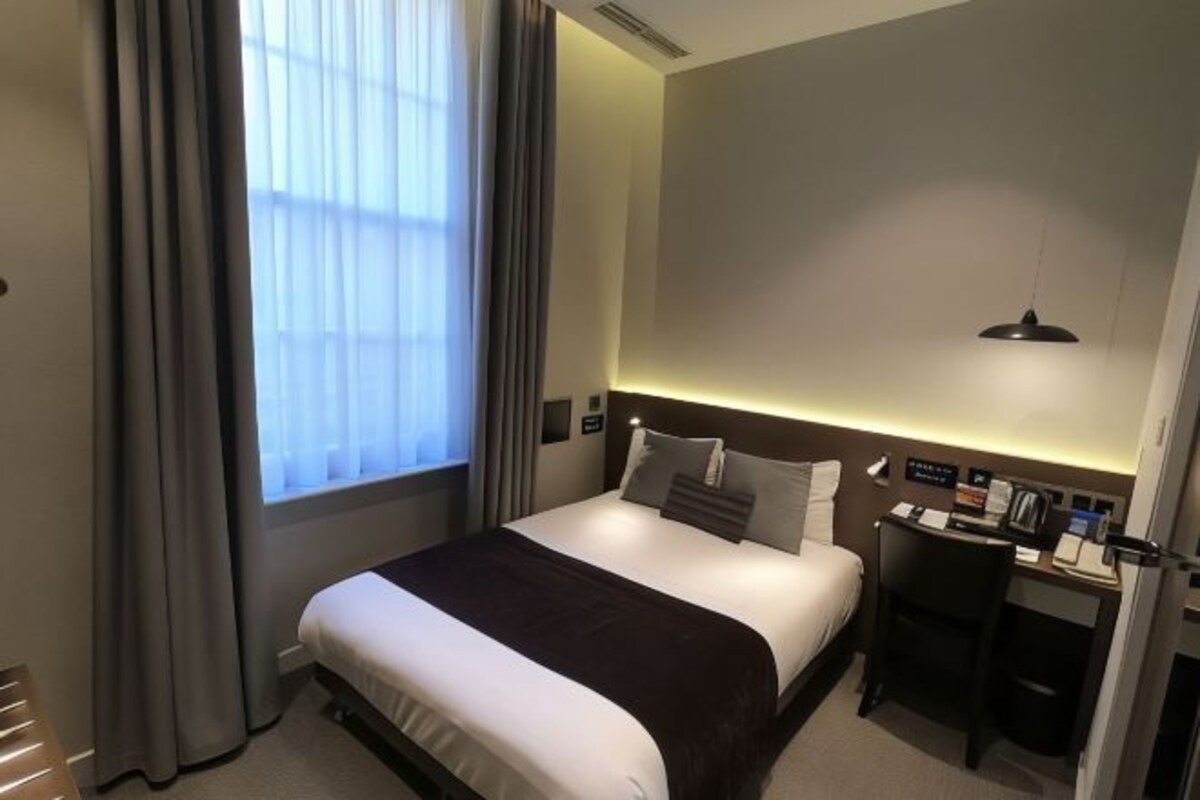 A hotel room with a bed, a desk, and a window with curtains.