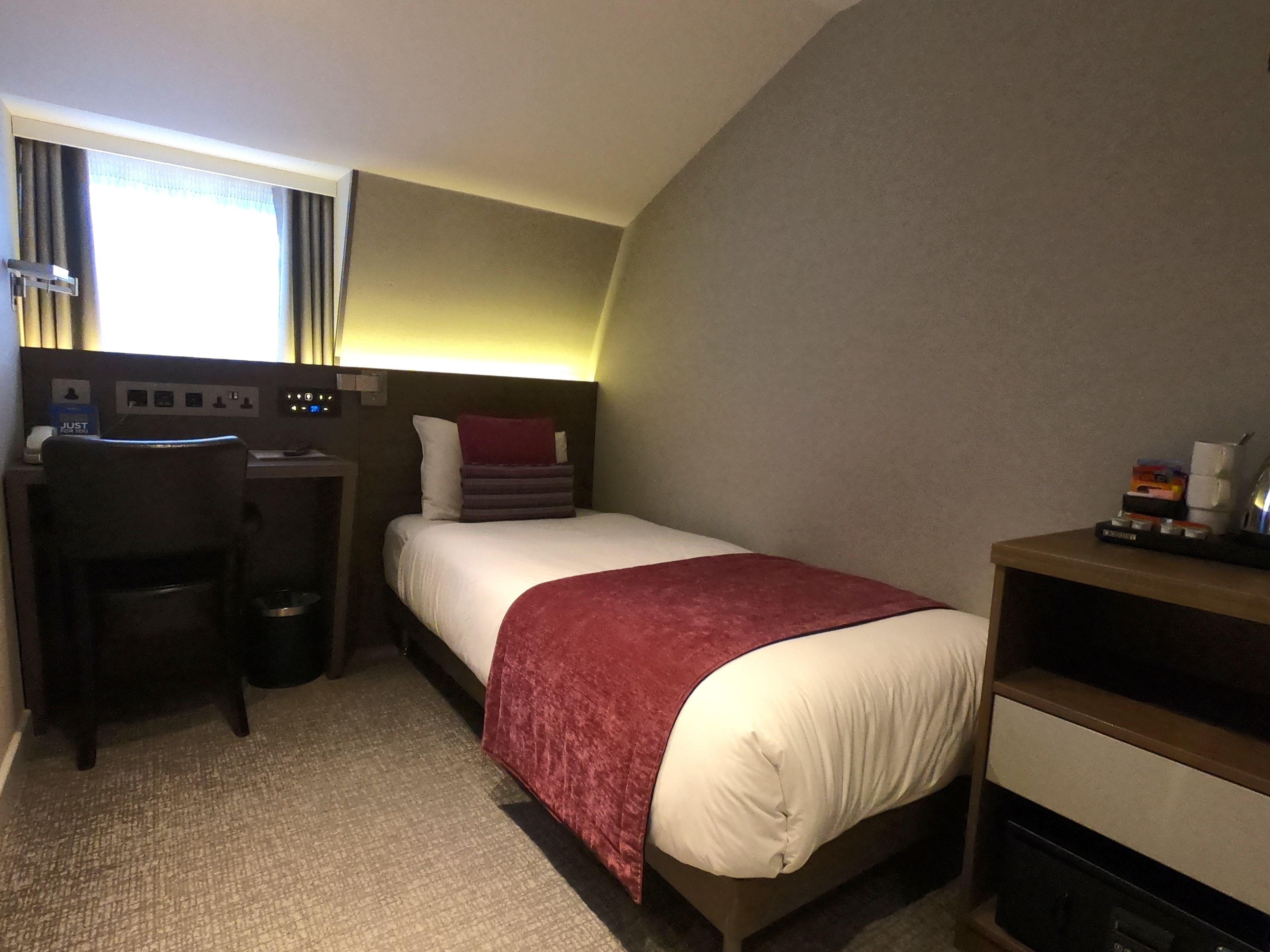 Une chambre d’hôtel avec un lit, un bureau, une chaise et une petite table avec une lampe.