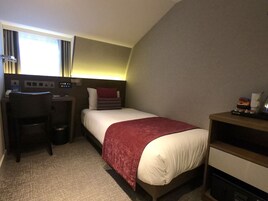 Una camera d'albergo con un letto, una scrivania, una sedia e un piccolo tavolo con una lampada.