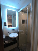 A modern bathroom with a glass-enclosed shower, a white sink, and a mirror with built-in lighting.