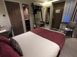 A hotel room with a bed, a desk with a telephone, a chair, a mirror, and a wardrobe.