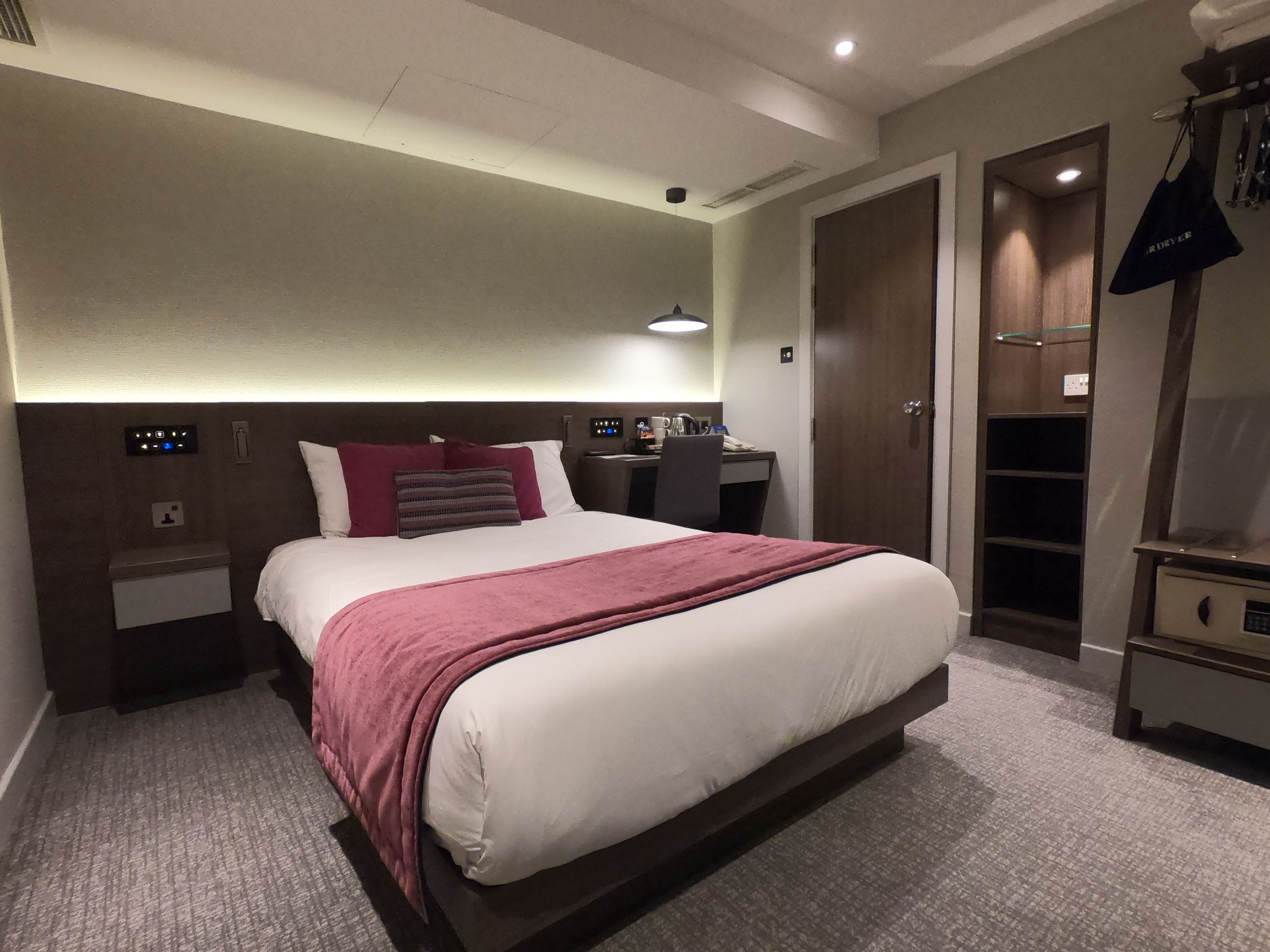 A hotel room with a large bed, a desk, a wardrobe, and a closet.