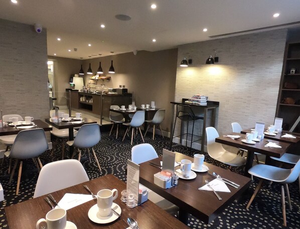 A modern hotel dining area with multiple tables and chairs, a coffee station, and a bar area.