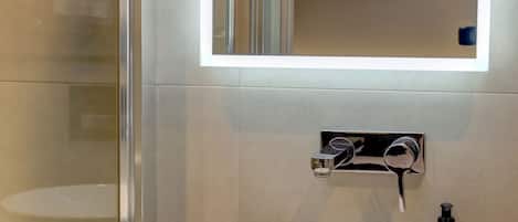 Un baño moderno con un lavabo blanco, un espejo y una cabina de ducha de vidrio.