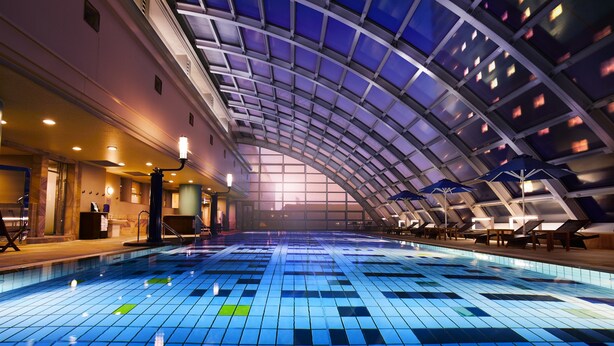 Una amplia piscina interior con un techo alto y arqueado y suelo de baldosas azules.