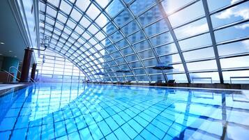 An indoor swimming pool with a glass ceiling, allowing natural light and views of the cityscape.