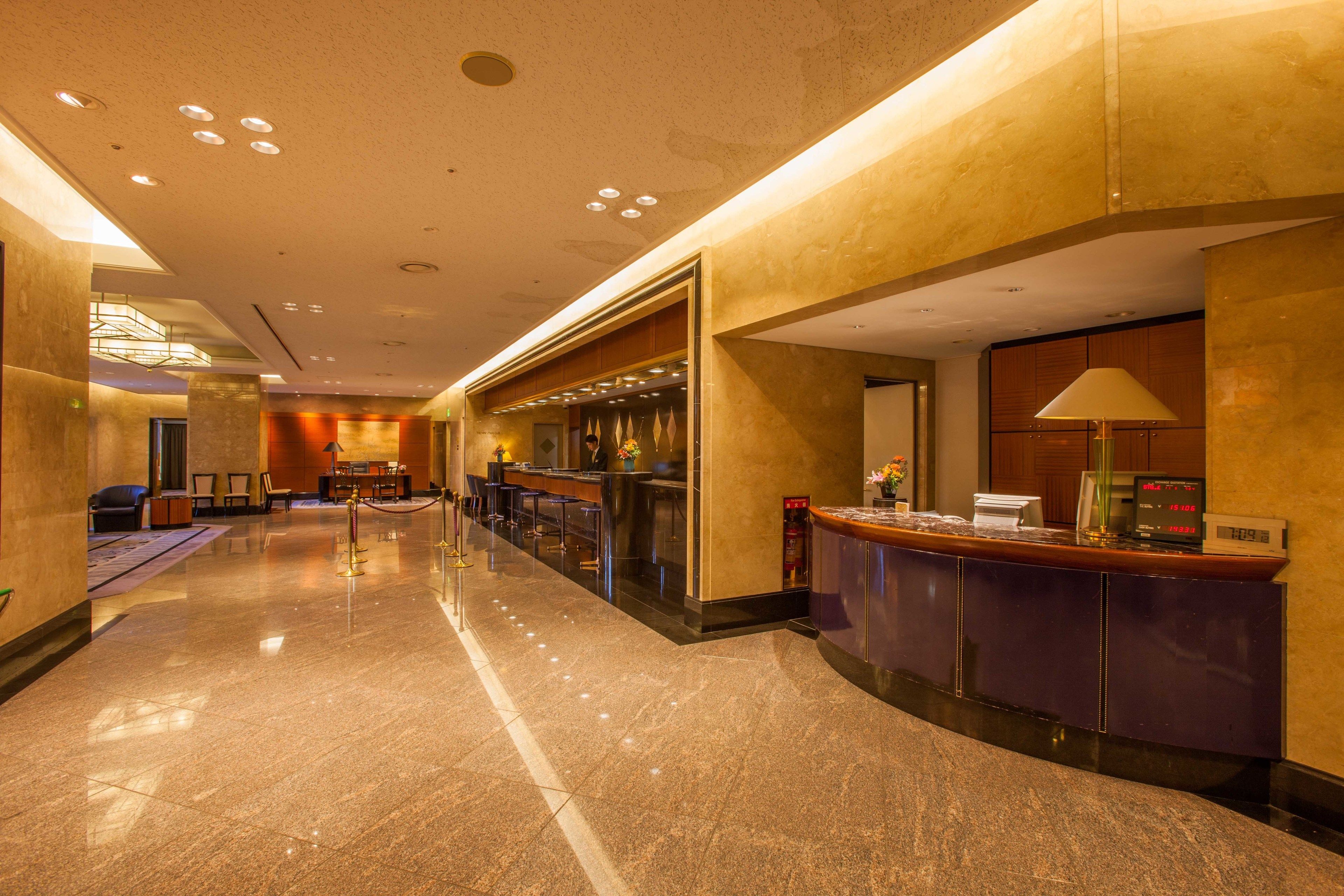 Um saguão de hotel com balcão de recepção, área de estar e um lustre moderno.