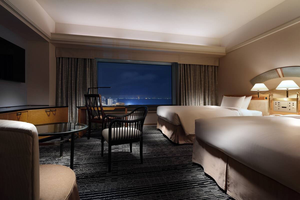 Hotelkamer met een groot bed, een bureau met stoel, een televisie en uitzicht op de stad 's nachts.