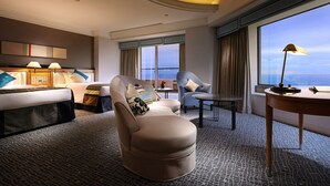 Una habitación de hotel moderna con una cama grande, un sofá, una silla, una mesita y vistas a la ciudad.