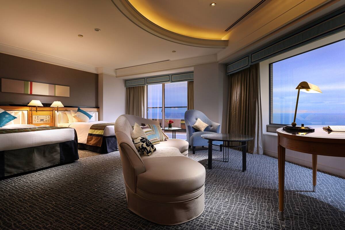 Een moderne hotelkamer met een groot bed, een bank, een stoel, een kleine tafel en uitzicht op de stad.