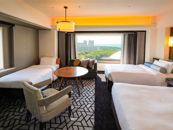 Une chambre d’hôtel avec deux lits, un canapé, une table ronde et une vue sur le paysage urbain.